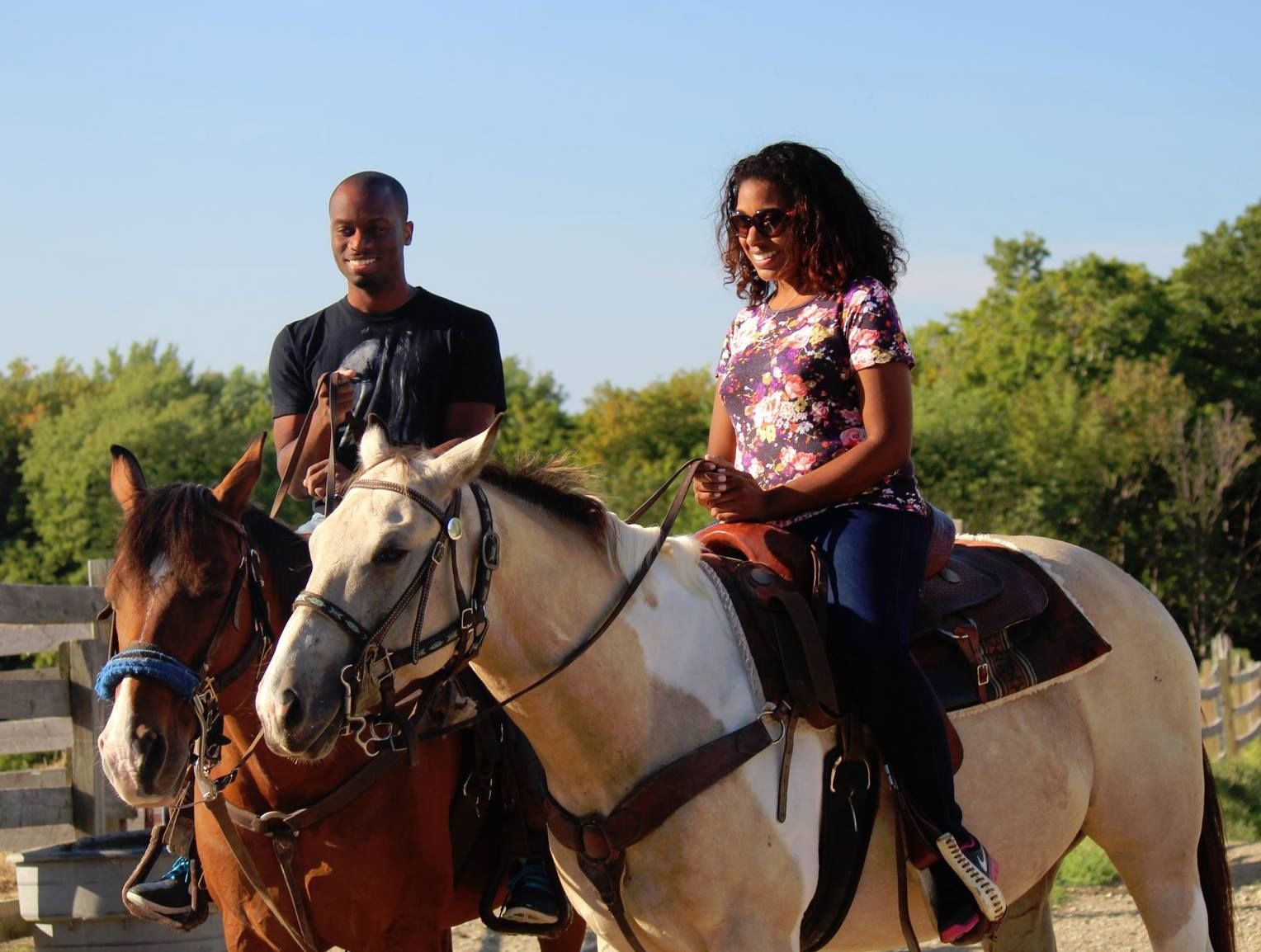 A man and a woman are riding horses in a fenced in area.