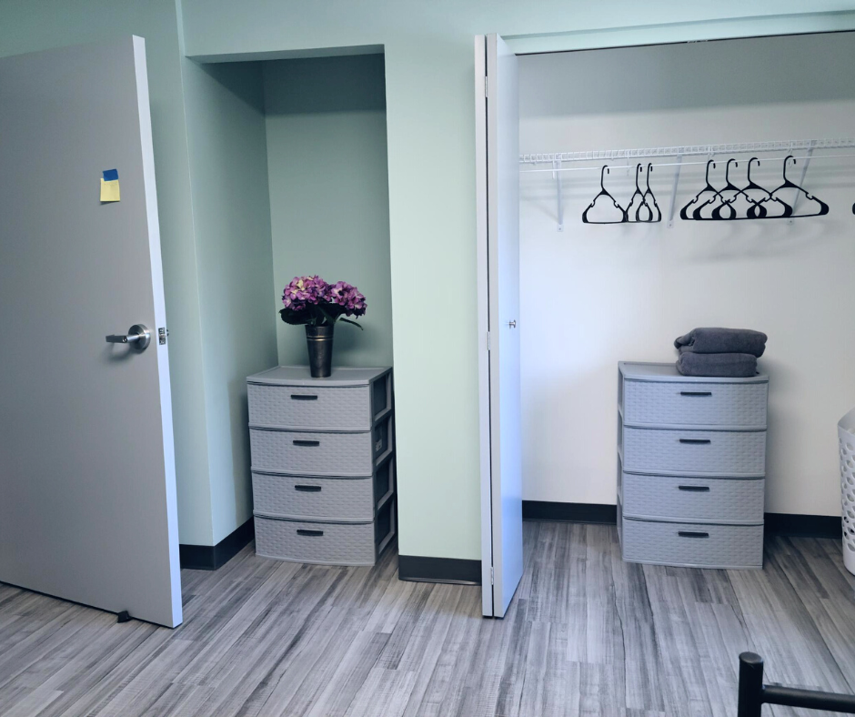 A room with a door, closet, and two gray drawer units. One has flowers; the other has towels.