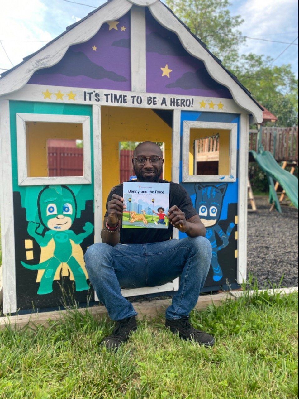 Man in front of colorful playhouse holding a book, featuring cartoon characters.