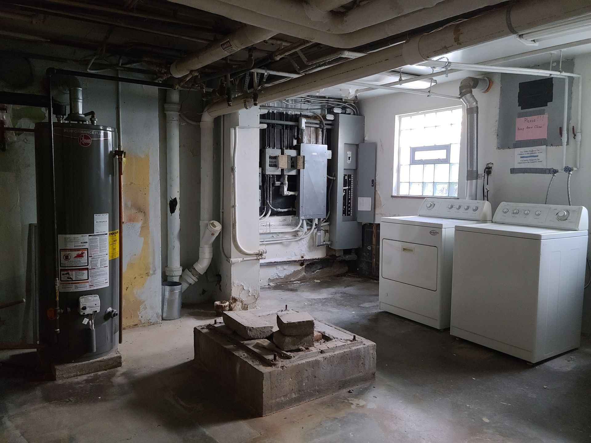 Basement with a water heater, electrical panel, washer, and dryer. Concrete floor, pipes overhead, and a small window.