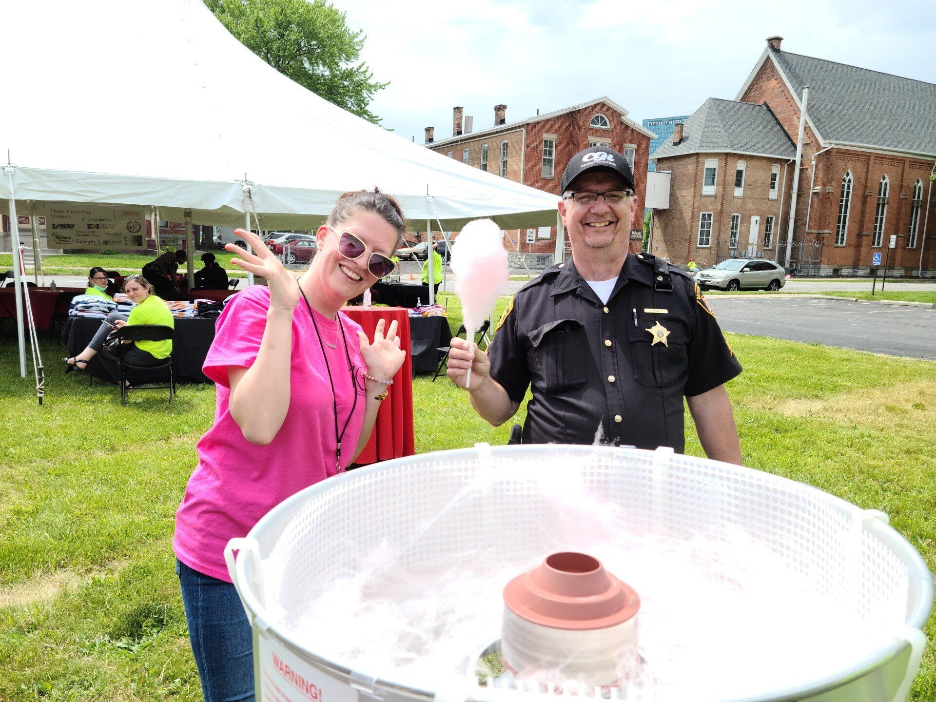 Woman and police officer with cotton candy, smiling, at outdoor event.