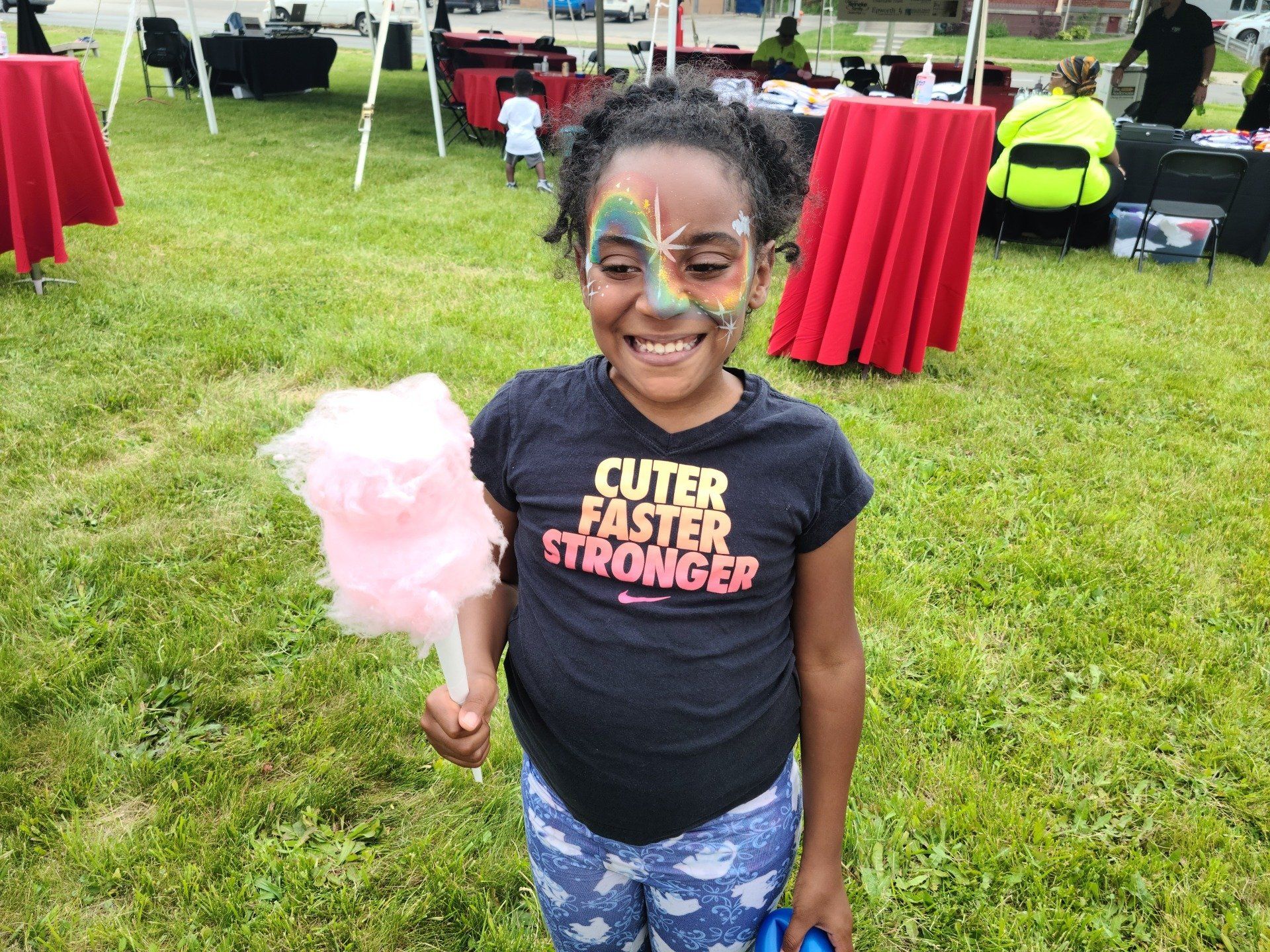 Girl with face paint and cotton candy smiles outside at an event.