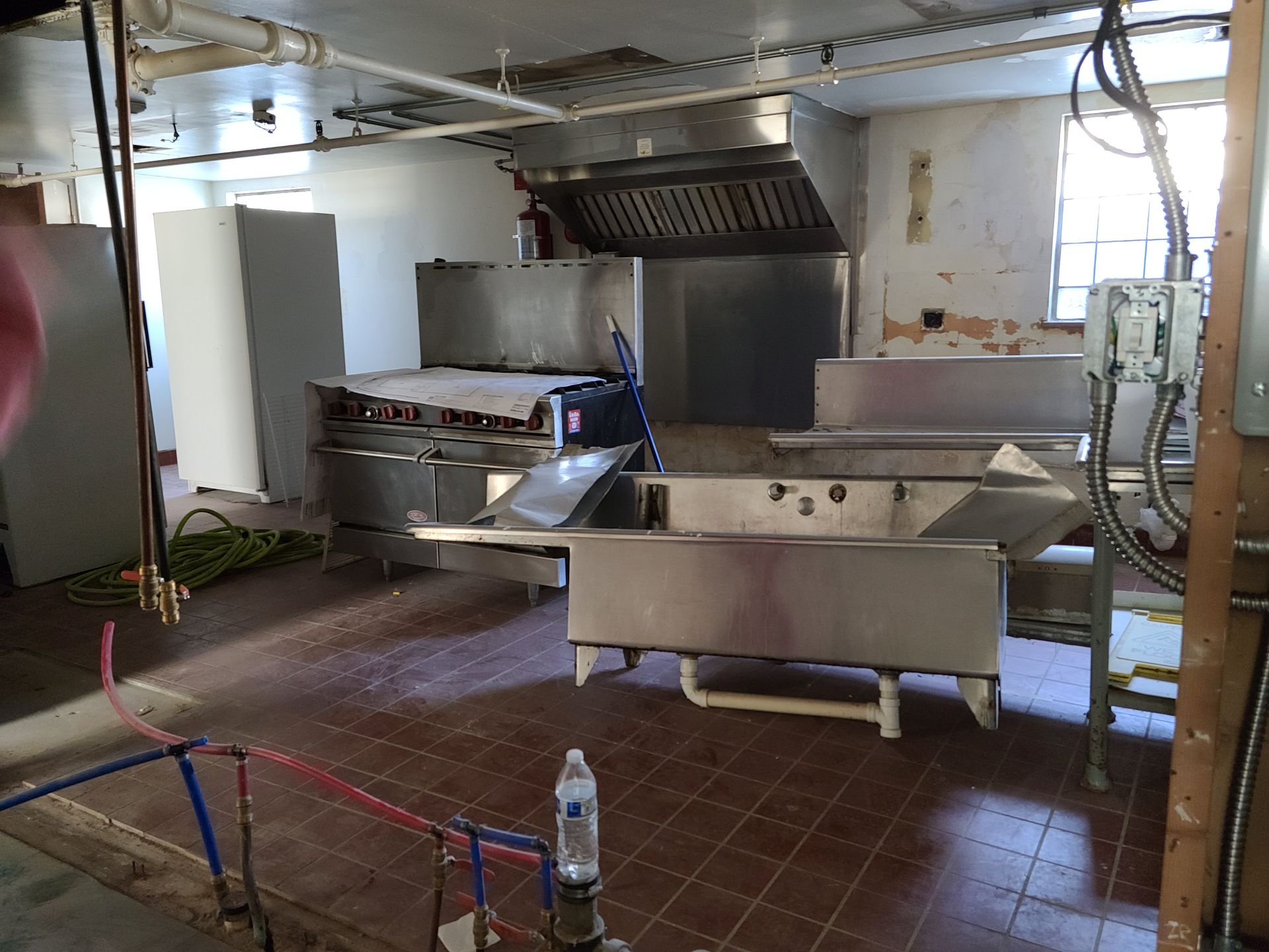 A commercial kitchen with stainless steel sinks, a ventilation hood, and unfinished walls.