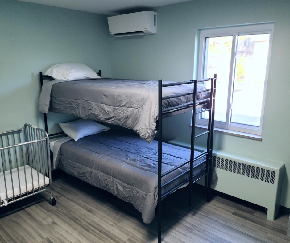 Bunk beds in a light-green room with a crib and window; air conditioner above.