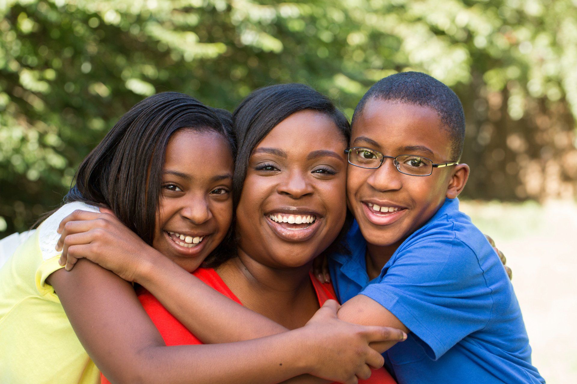 A woman and two children are hugging each other in a park.