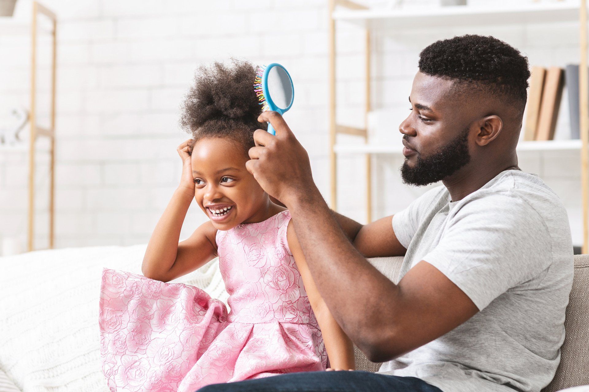 A man is brushing a little girl 's hair while sitting on a couch.