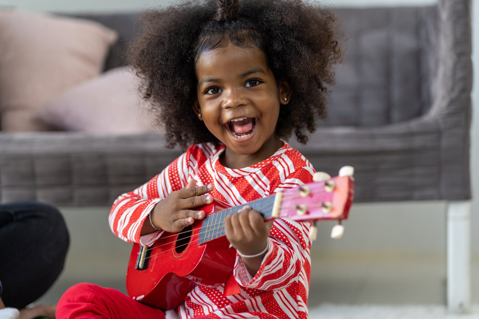 A little girl is sitting on the floor playing a guitar.