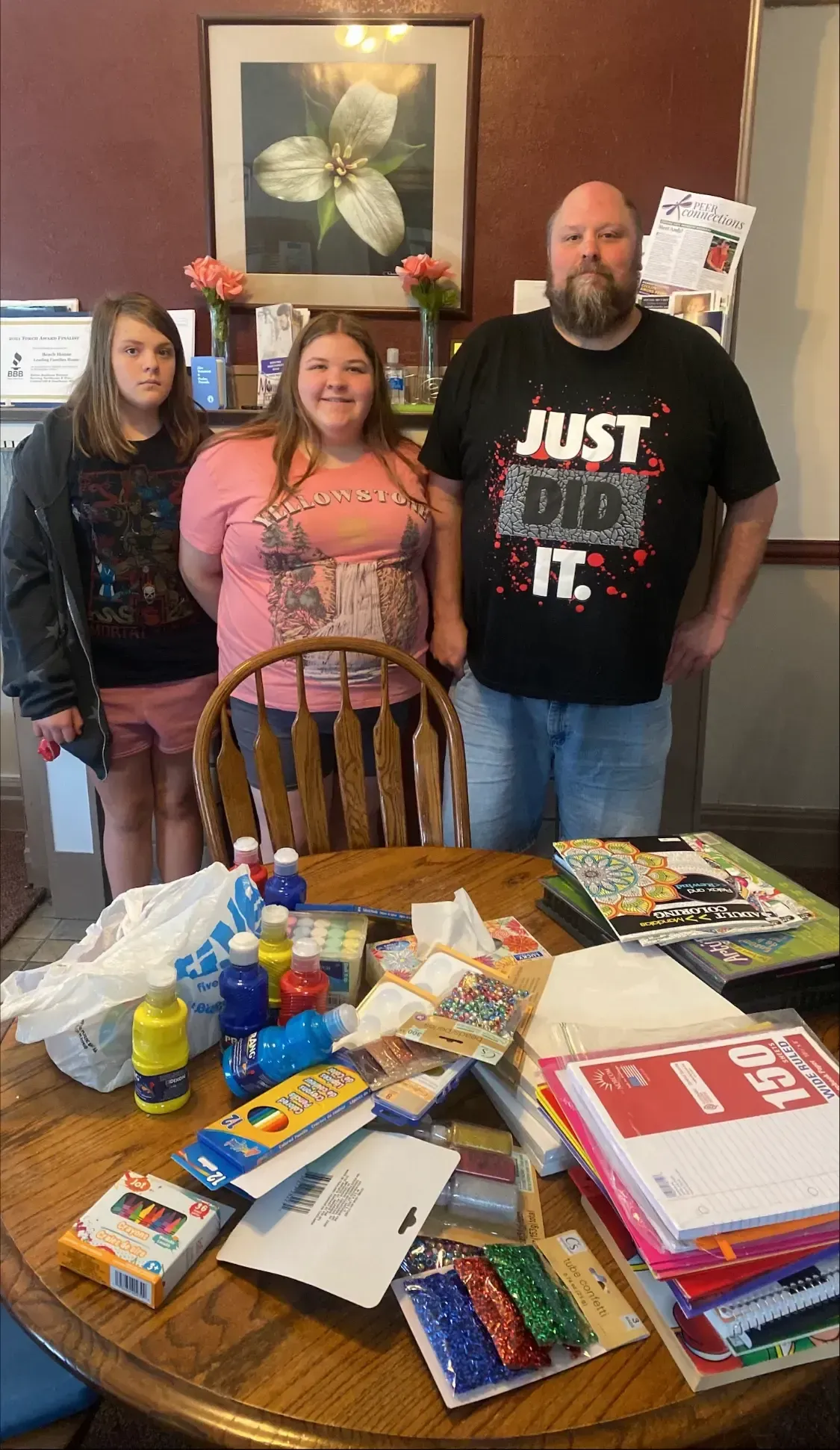 Family, smiling, stands behind a table of school supplies. Man wears a