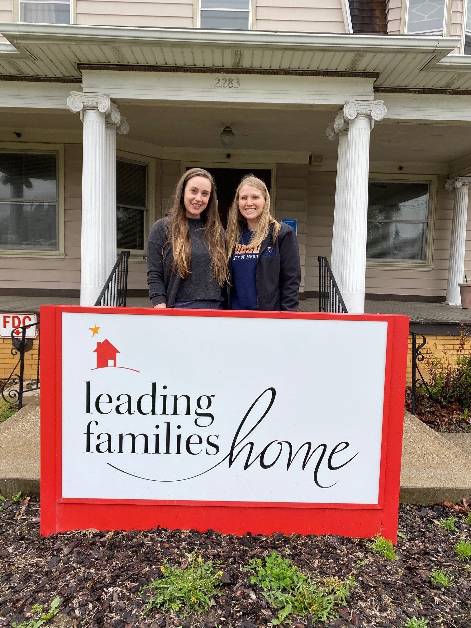 Two women stand behind a red sign for