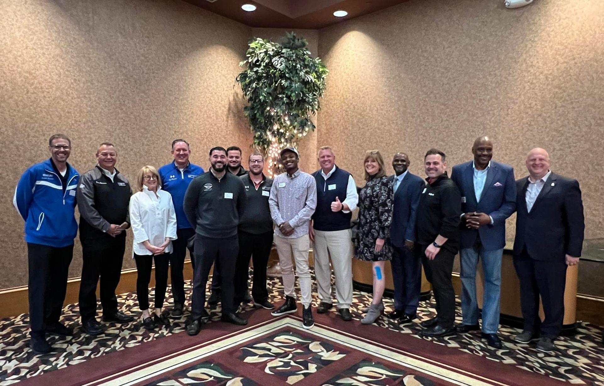 Group of people posing for a photo in a room with patterned carpet. Several are smiling, and some are wearing suits.