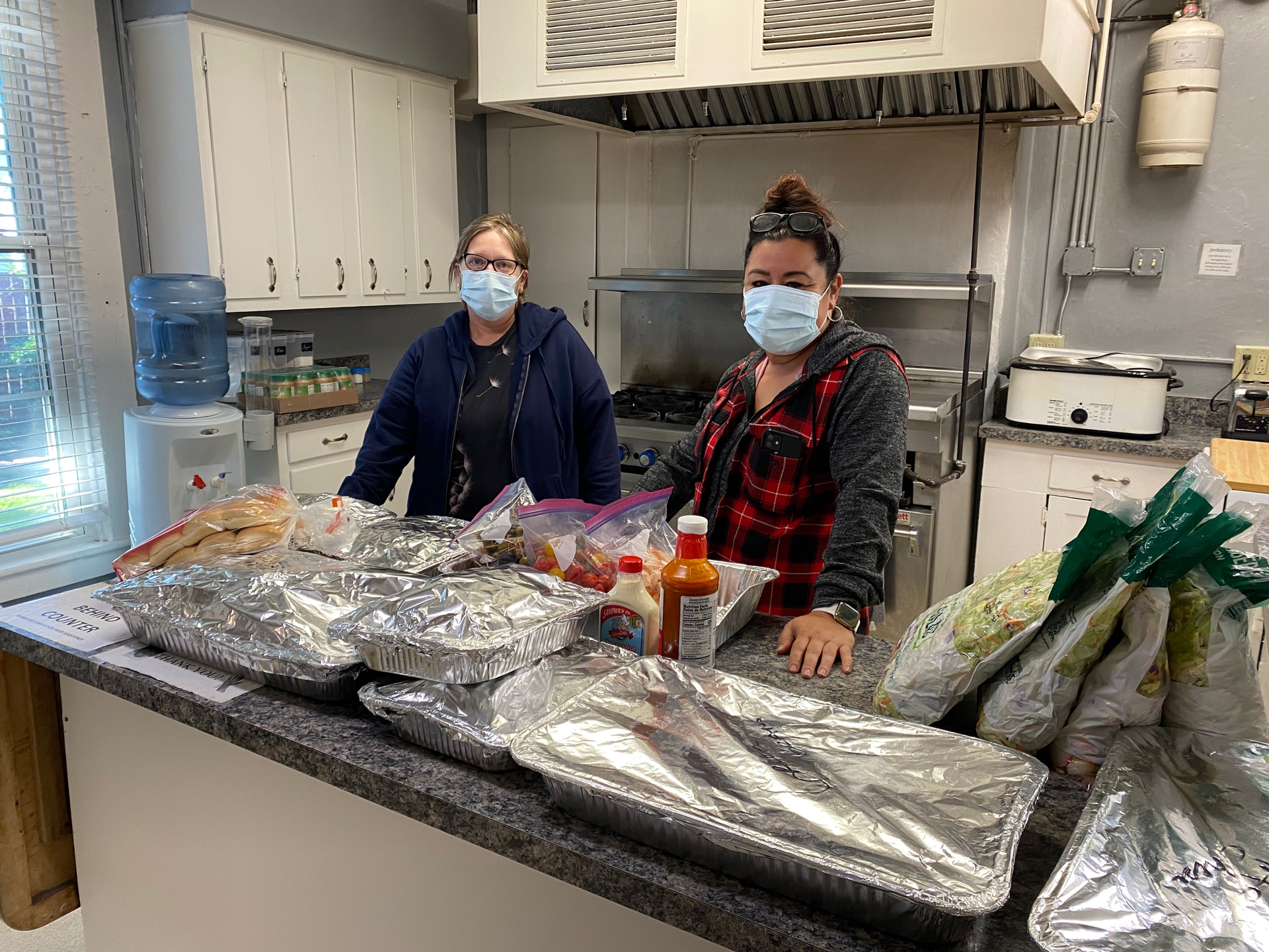 Two women wearing face masks are standing in a kitchen.