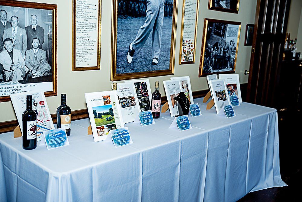 Table display with wine bottles, framed documents, and photos, under golf-themed decor.