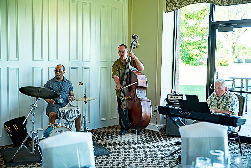 Jazz trio playing music indoors: drummer, bassist, and keyboardist.