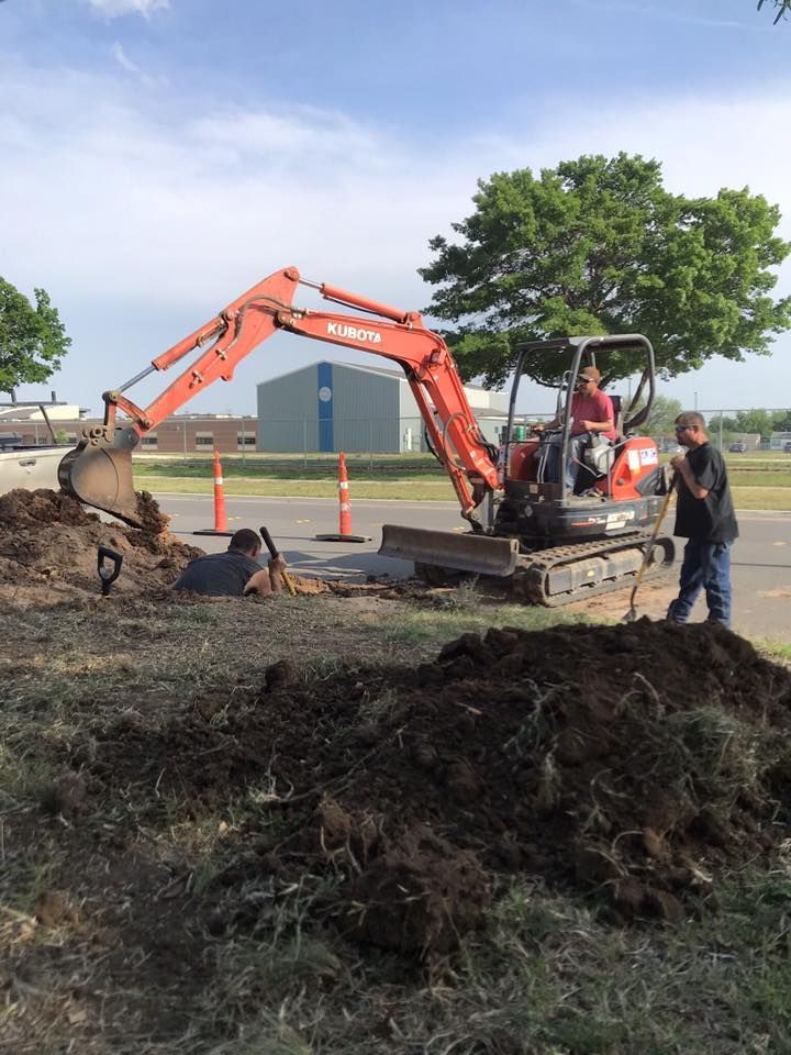 An orange excavator digging in dirt, two men working on a sunny day.