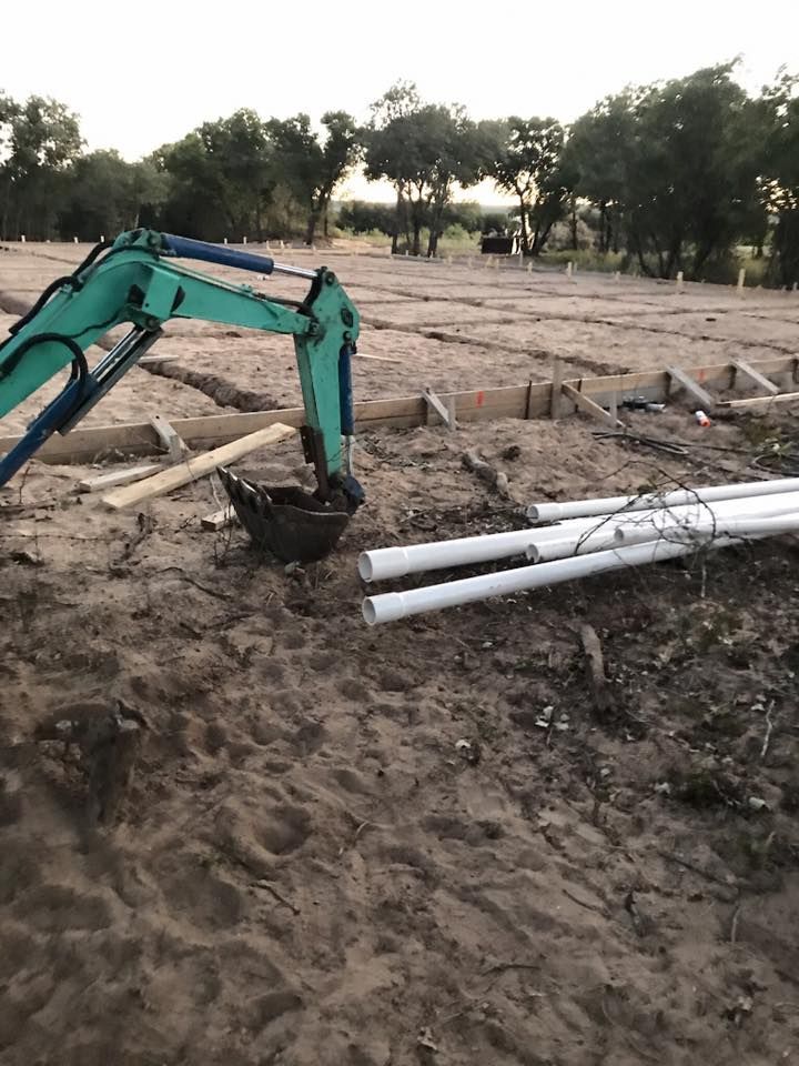Mini excavator digging in dirt near white pipes and wooden forms on a construction site.