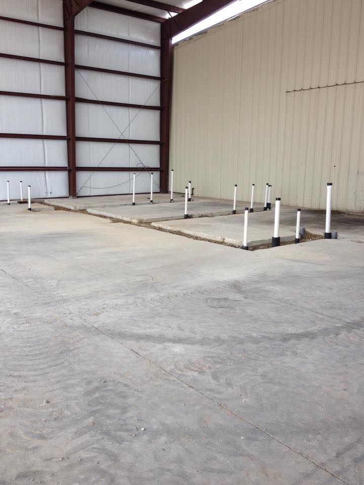 Concrete floor with white pipes and concrete platforms inside a metal-framed building.
