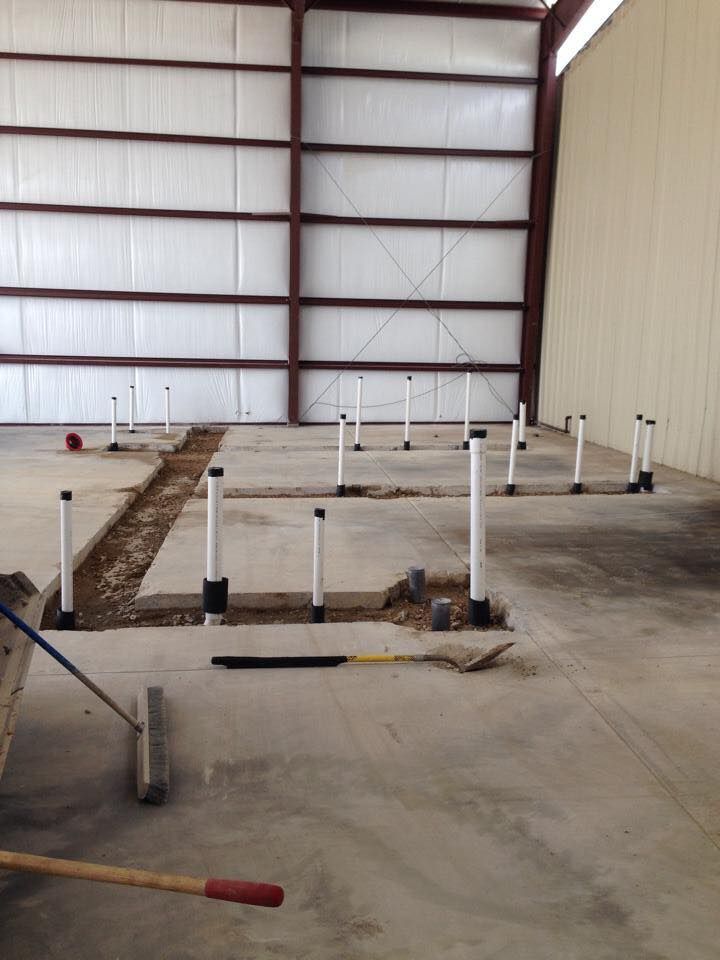 Interior view of a building under construction, showing exposed plumbing pipes in a concrete floor.