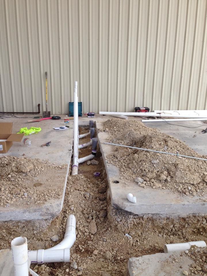 Construction site with plumbing pipes installed in a trench. Beige wall in the background.