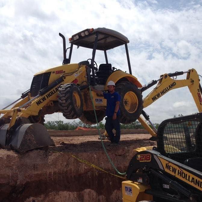 Man stands near a New Holland backhoe excavator and skid steer on a construction site.