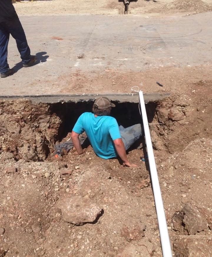 A person in a turquoise shirt crawls into a dirt hole dug in the side of a road.