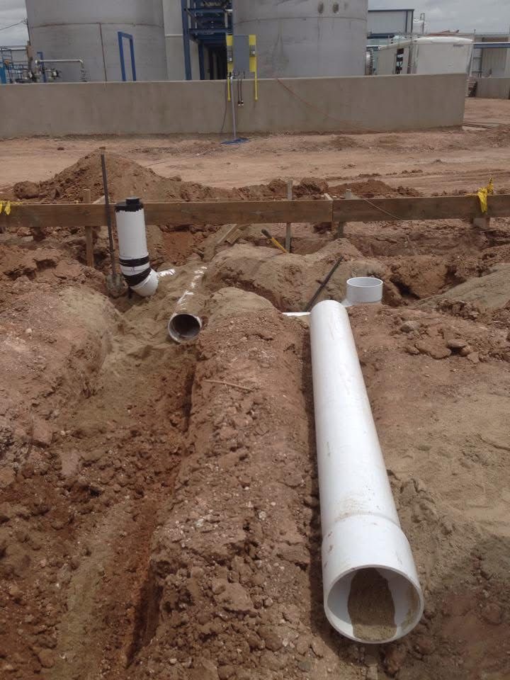 Construction site with trenches and white PVC pipes for plumbing.
