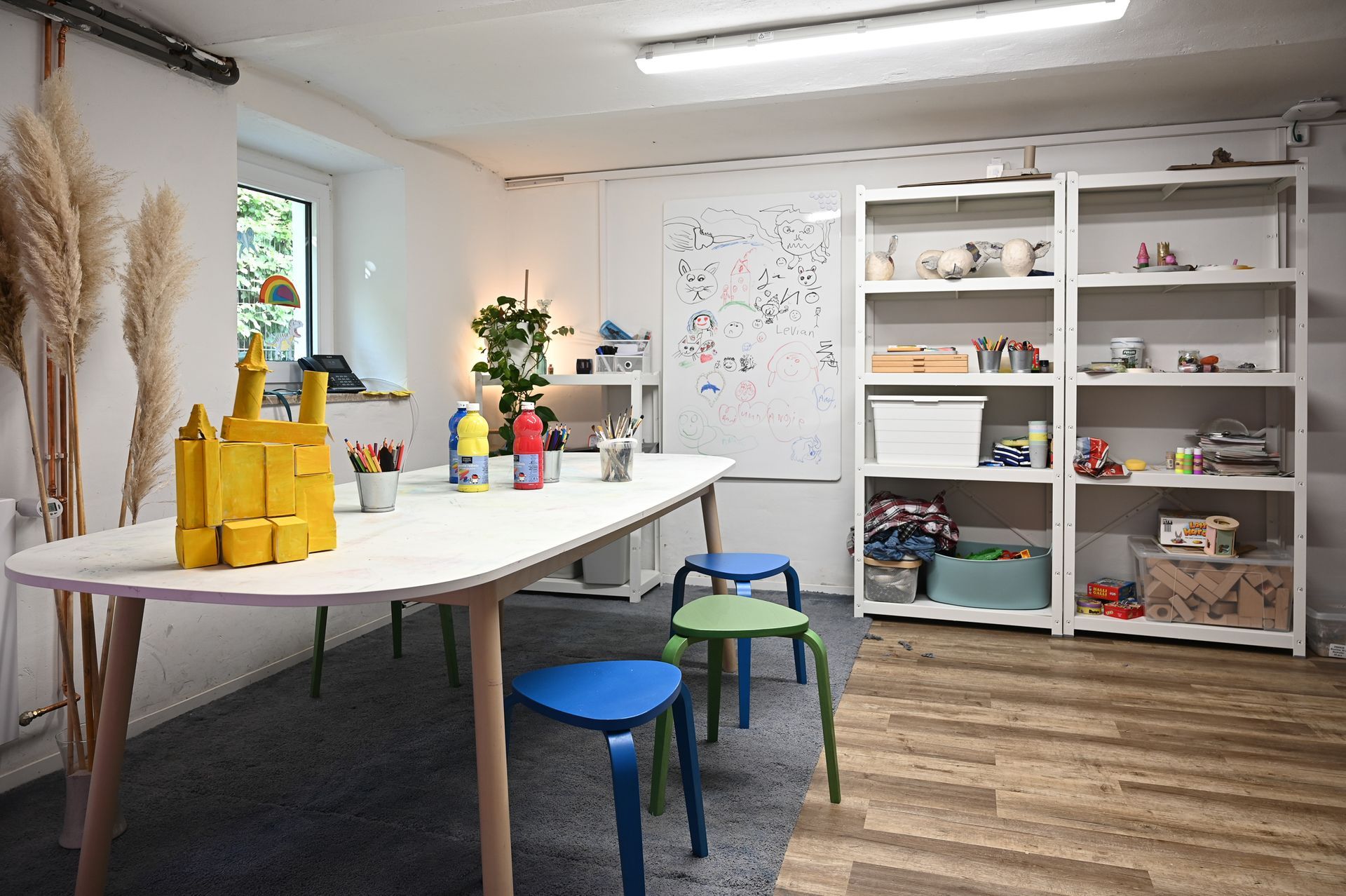 Ein Kunstraum mit Tisch, Hockern, Regalen und Spielzeug. Der Boden besteht aus Holz und Teppich. Kirstin Hammerstein, hammerstein-pictures