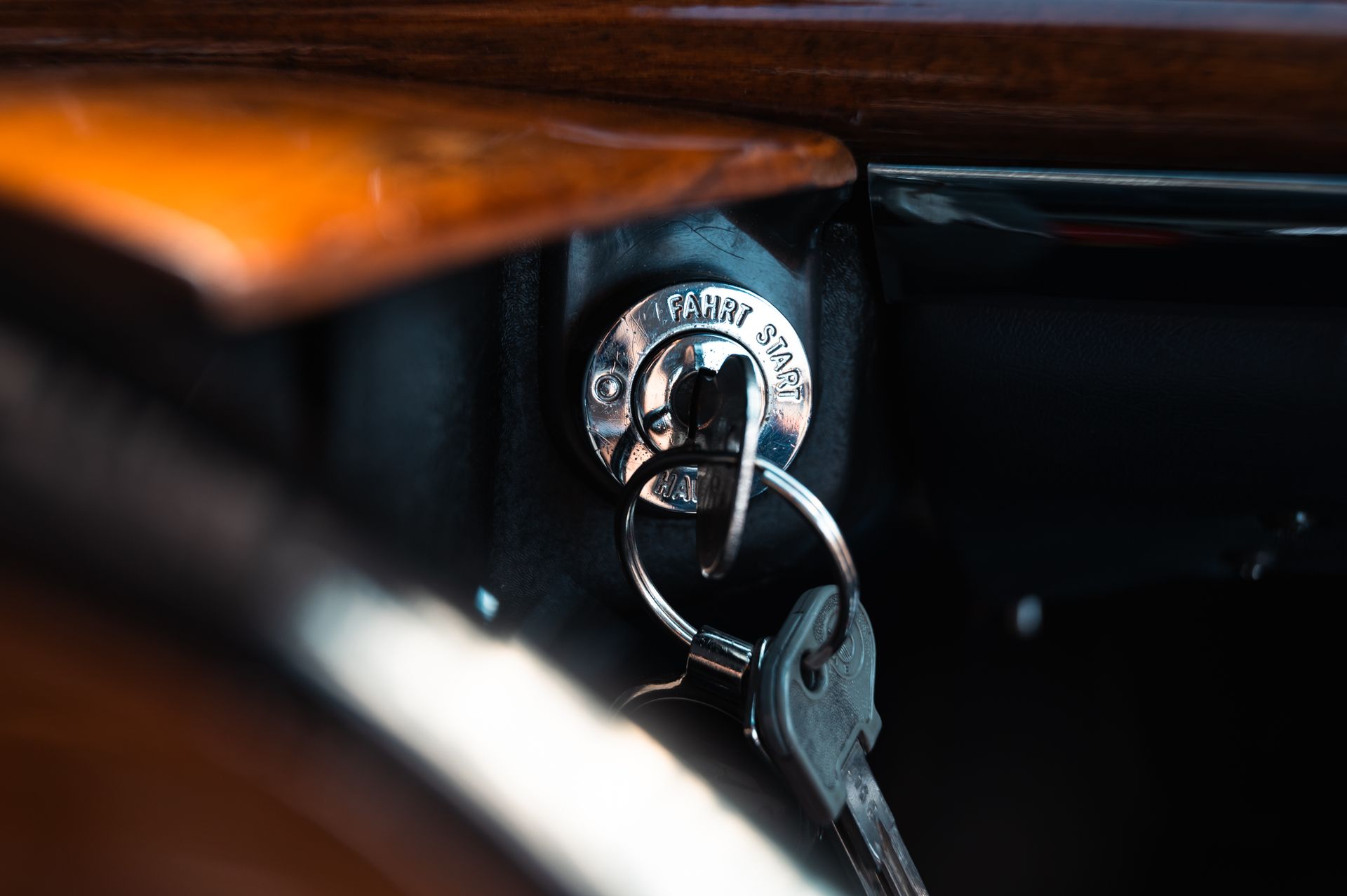 Ein silberner Schlüssel steckt in der Zündung eines Autos. Die Schlüssel hängen am Schlüsselring, daneben befindet sich ein hölzernes Armaturenbrett. Kirstin Hammerstein, hammerstein-pictures