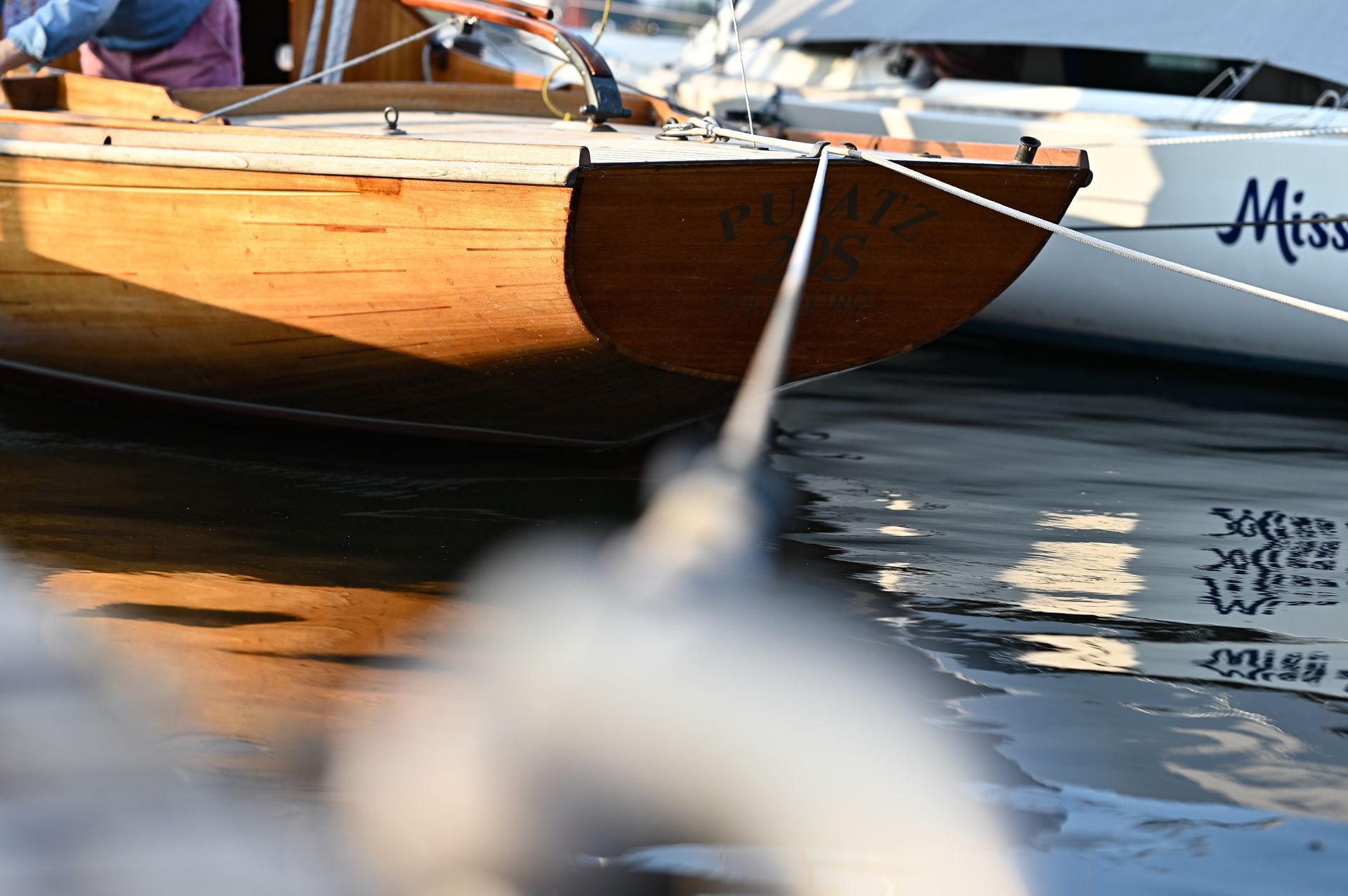 Ein hölzernes Segelboot, das mit einem weißen Seil an einem Dock festgemacht ist. Das Licht wird auf dem Wasser reflektiert. Kirstin Hammerstein, hammerstein-pictures