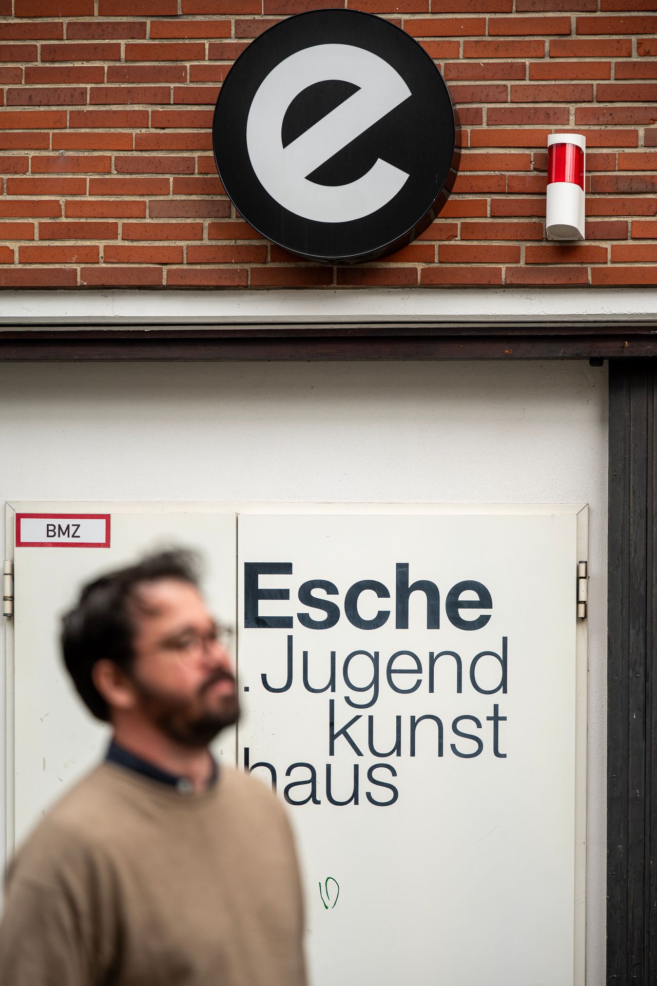Schild für „Esce Jugendkunsthaus“ mit einer verschwommenen Person im Vordergrund. Das Schild zeigt ein großes „e“-Logo und Schriftzug auf weißem Hintergrund.