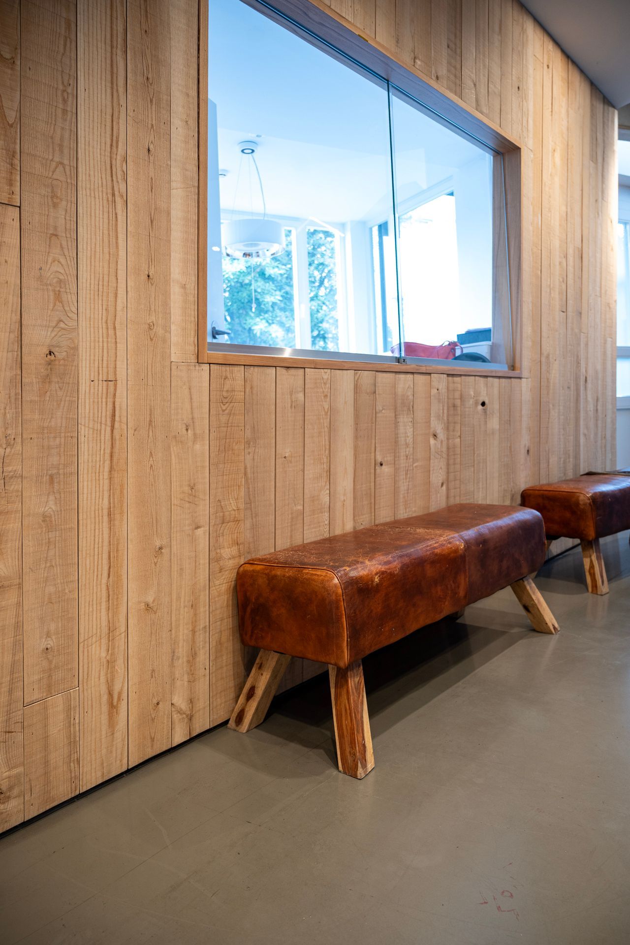 Zwei mit Leder bezogene Bänke vor einer holzgetäfelten Wand, unterhalb eines Fensters.