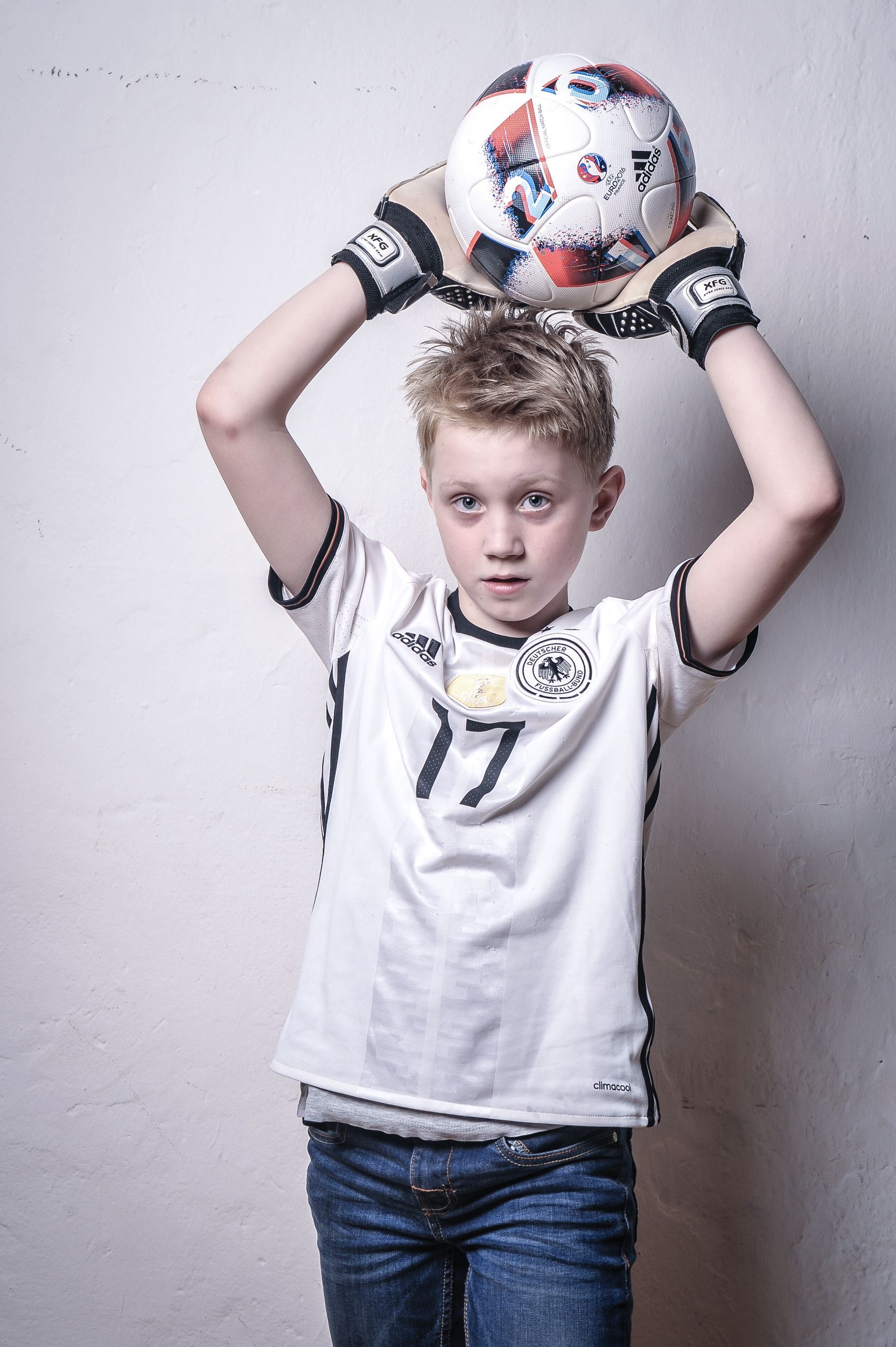 Junge im Fußballtrikot hält einen Fußball über dem Kopf und trägt Torwarthandschuhe. Kirstin Hammerstein, hammerstein-pictures