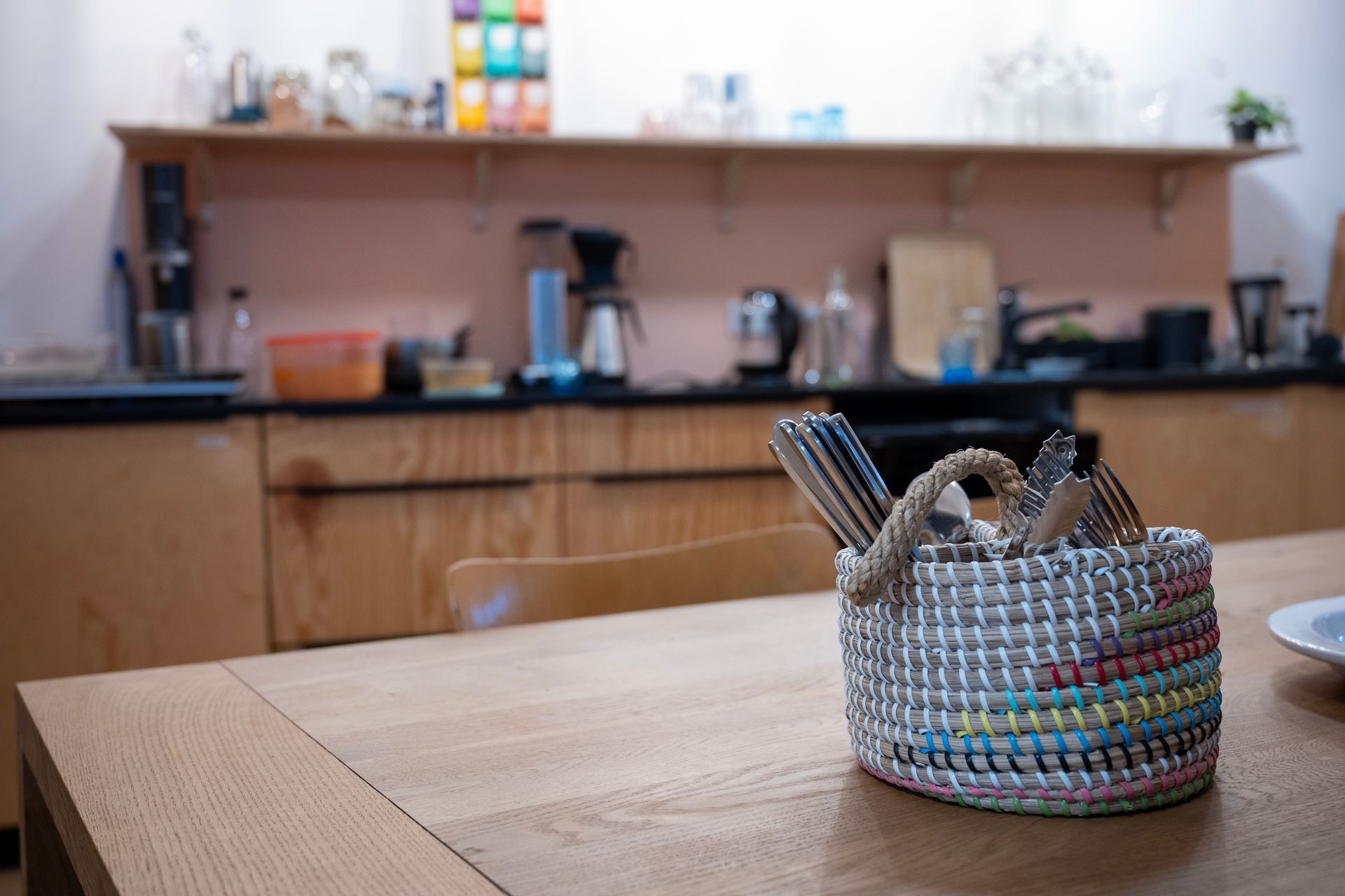 Ein Korb mit Silberbesteck auf einem Holztisch, im Hintergrund die Küche.