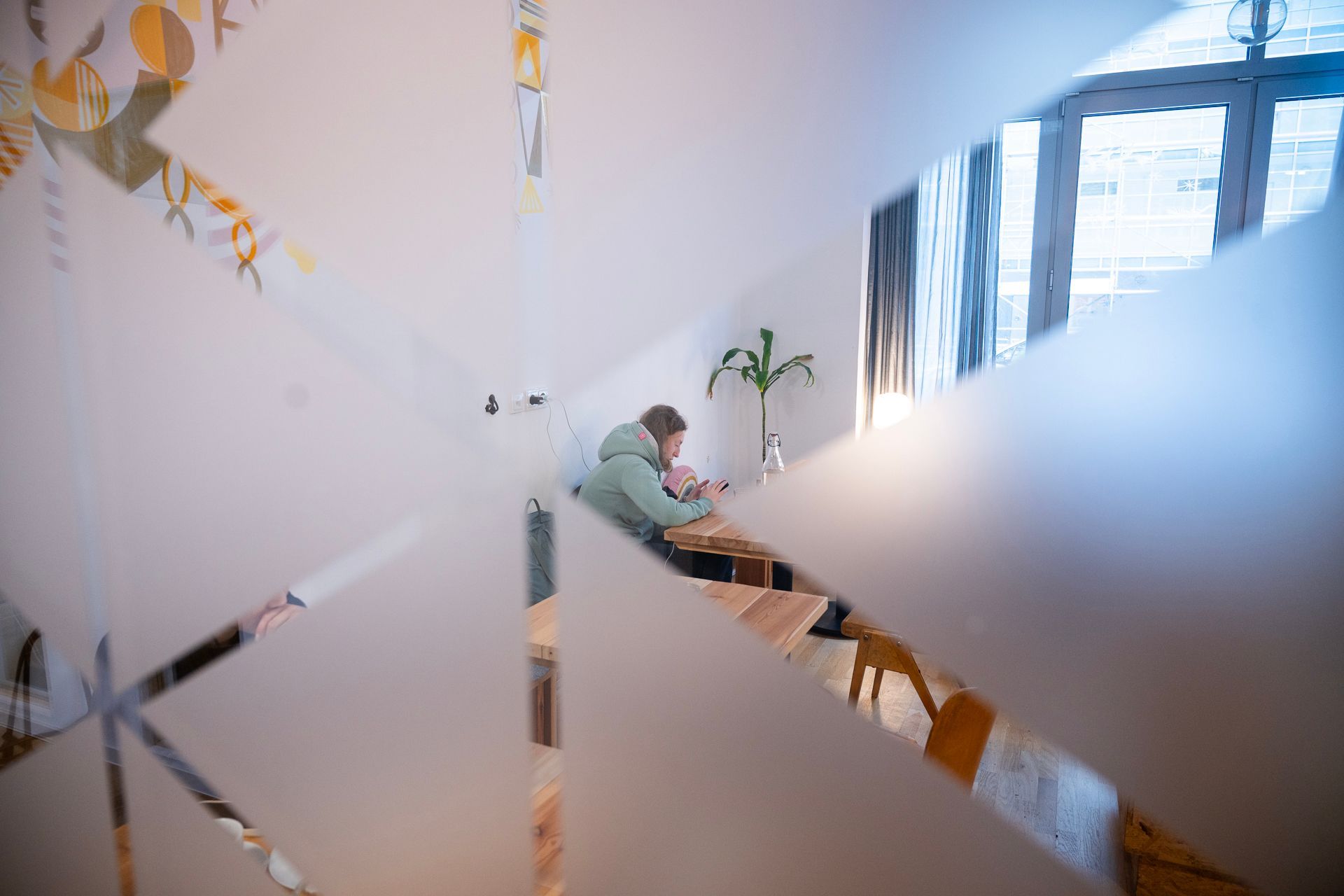 Eine Person sitzt an einem Tisch, gesehen durch ein Milchglasfenster mit geometrischen Mustern.