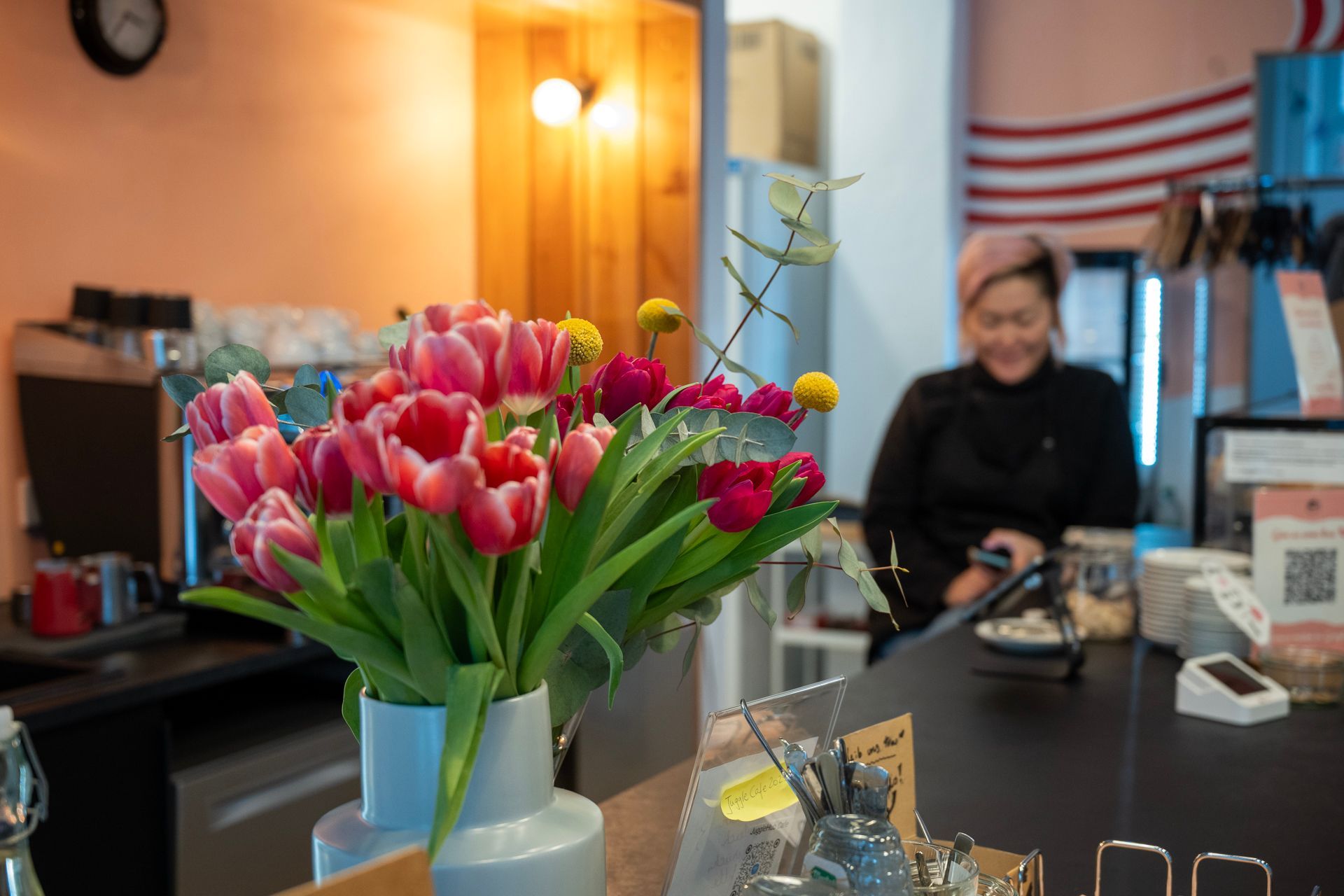 Ein Strauß rosa Tulpen auf einer Theke, dahinter eine verschwommene Person.