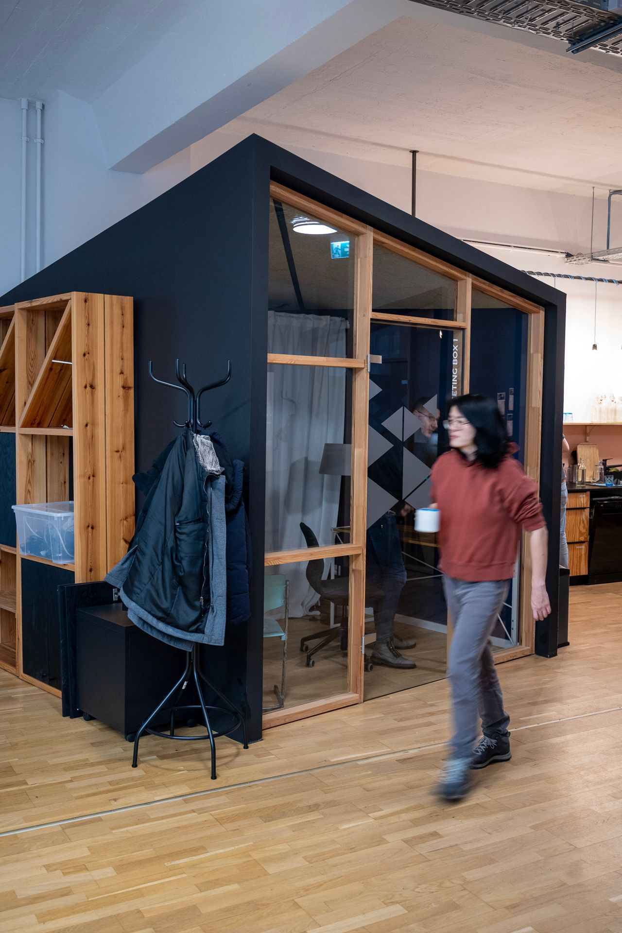 Eine Person geht an einer dunkelblauen Bürokabine mit Holzregalen vorbei.