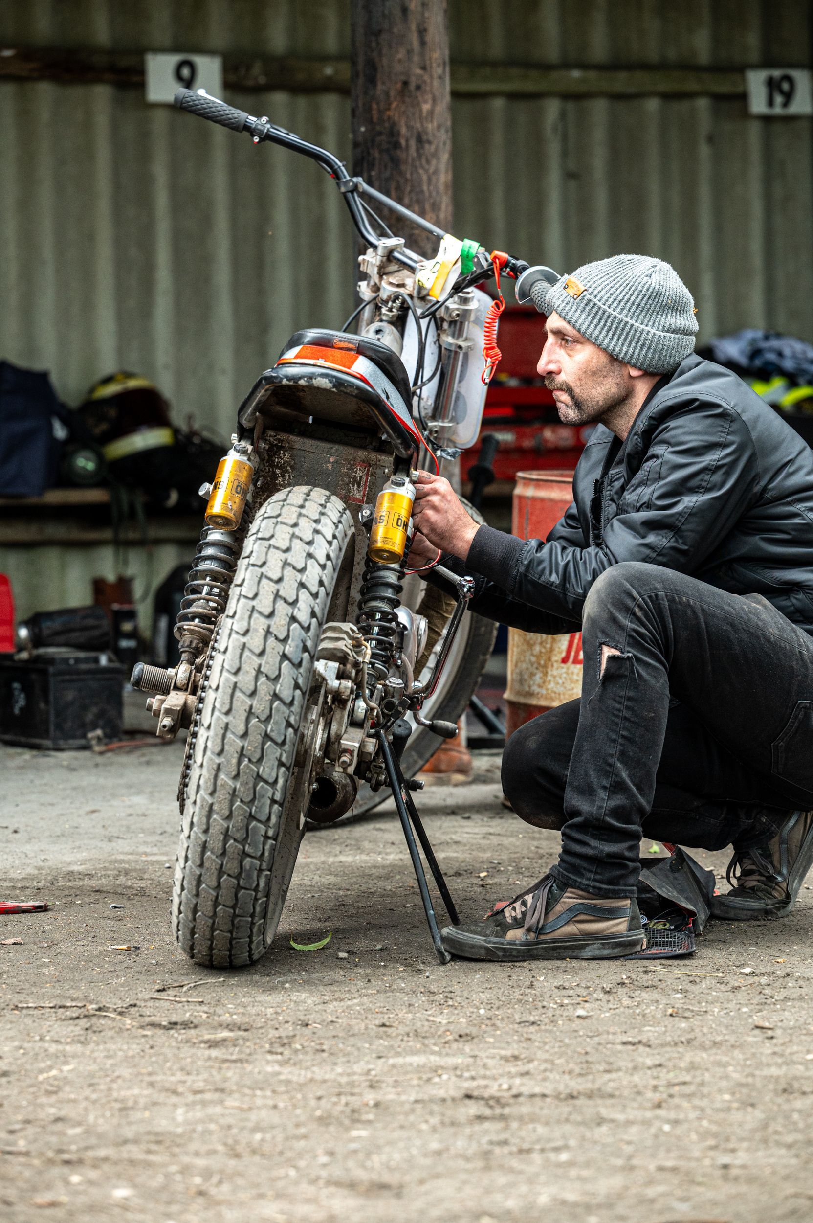 Mann mit Beanie hockt und stellt Motorrad in einer Garage ein. Kirstin Hammerstein, hammerstein-pictures