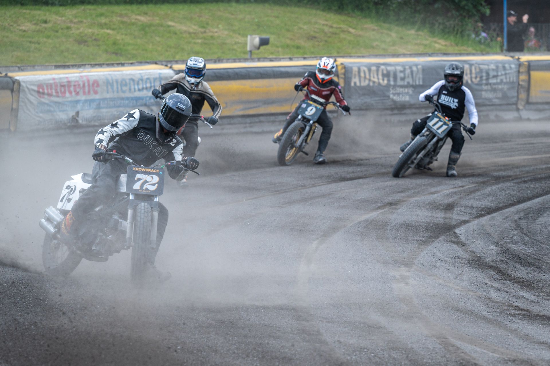Motorradrennfahrer auf einer unbefestigten Strecke, die Staub aufwirbeln. Vier Fahrer in Aktion, Helme und Lederkombis, Wettkampf. Kirstin Hammerstein, hammerstein-pictures