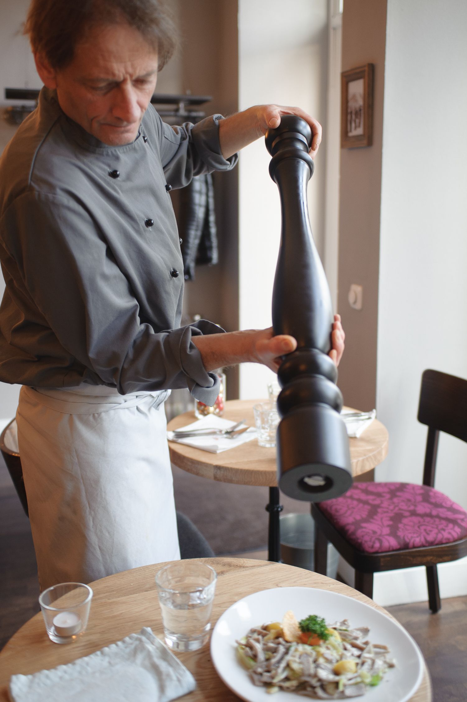 Koch mahlt in einem Restaurant Pfeffer auf einen Teller mit Essen. Kirstin Hammerstein, hammerstein-pictures