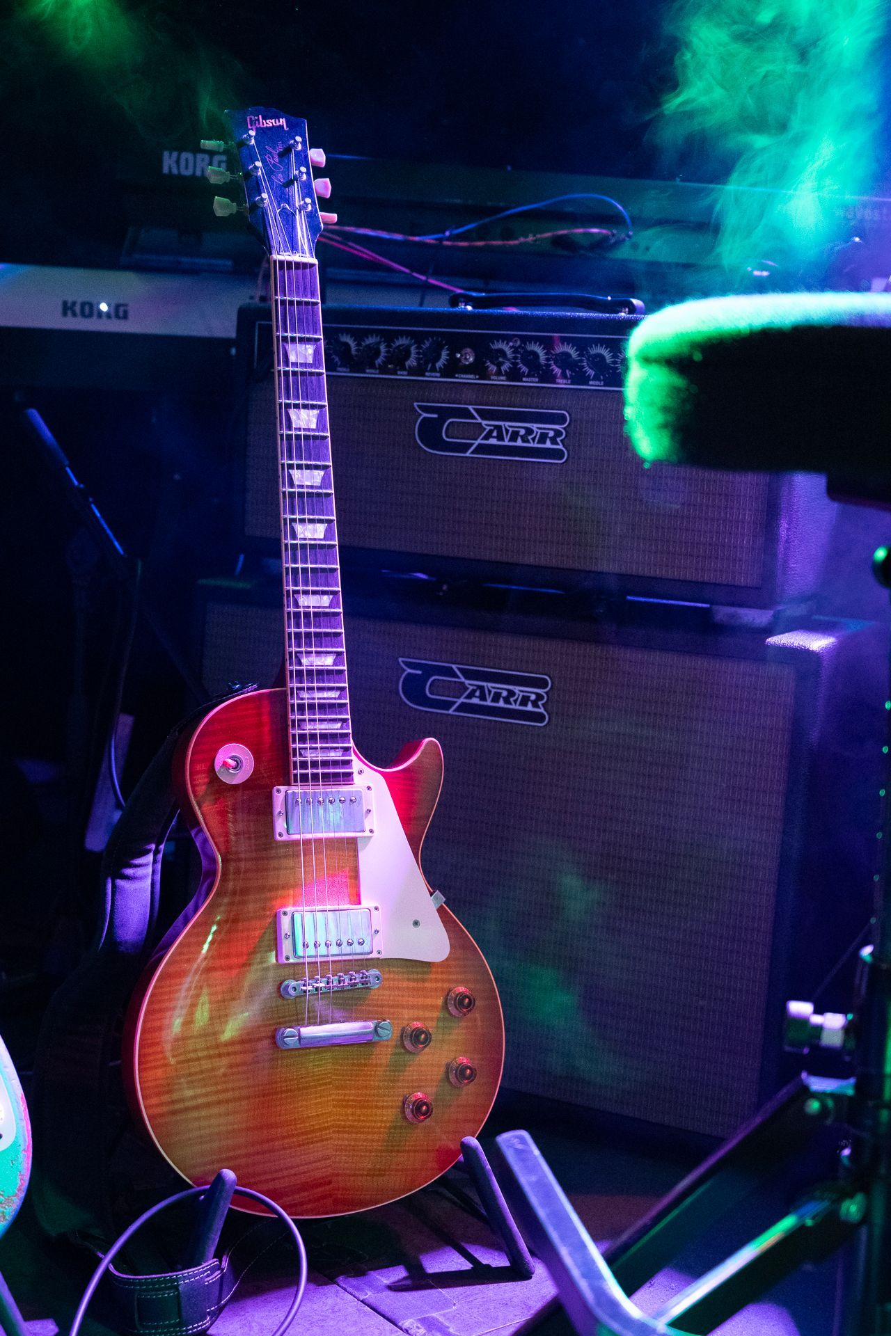 Eine Sunburst Les Paul-Gitarre lehnt an zwei braunen Gitarrenverstärkern. Bühnenbild mit blauer und grüner Beleuchtung.