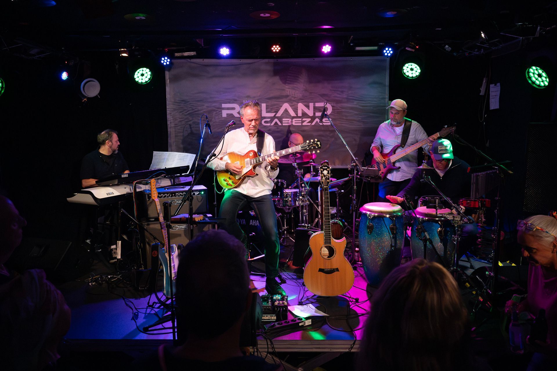 Bandauftritt auf der Bühne mit Lichteffekten und Banner, Gitarrist in der Mitte, Publikum im Vordergrund.