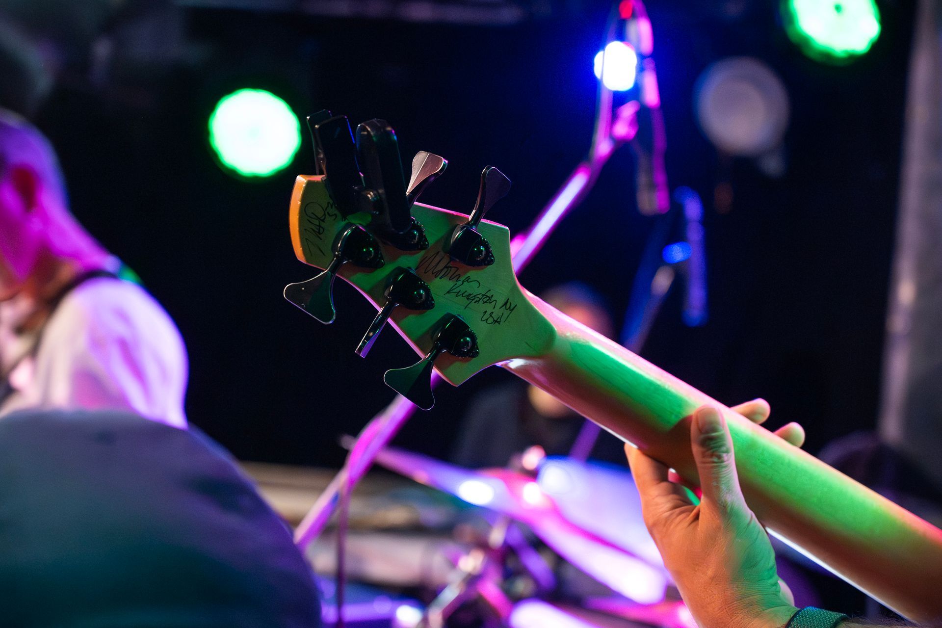 Im Fokus der Bassgitarre, gespielt auf der Bühne vor farbenfroher Bühnenbeleuchtung.