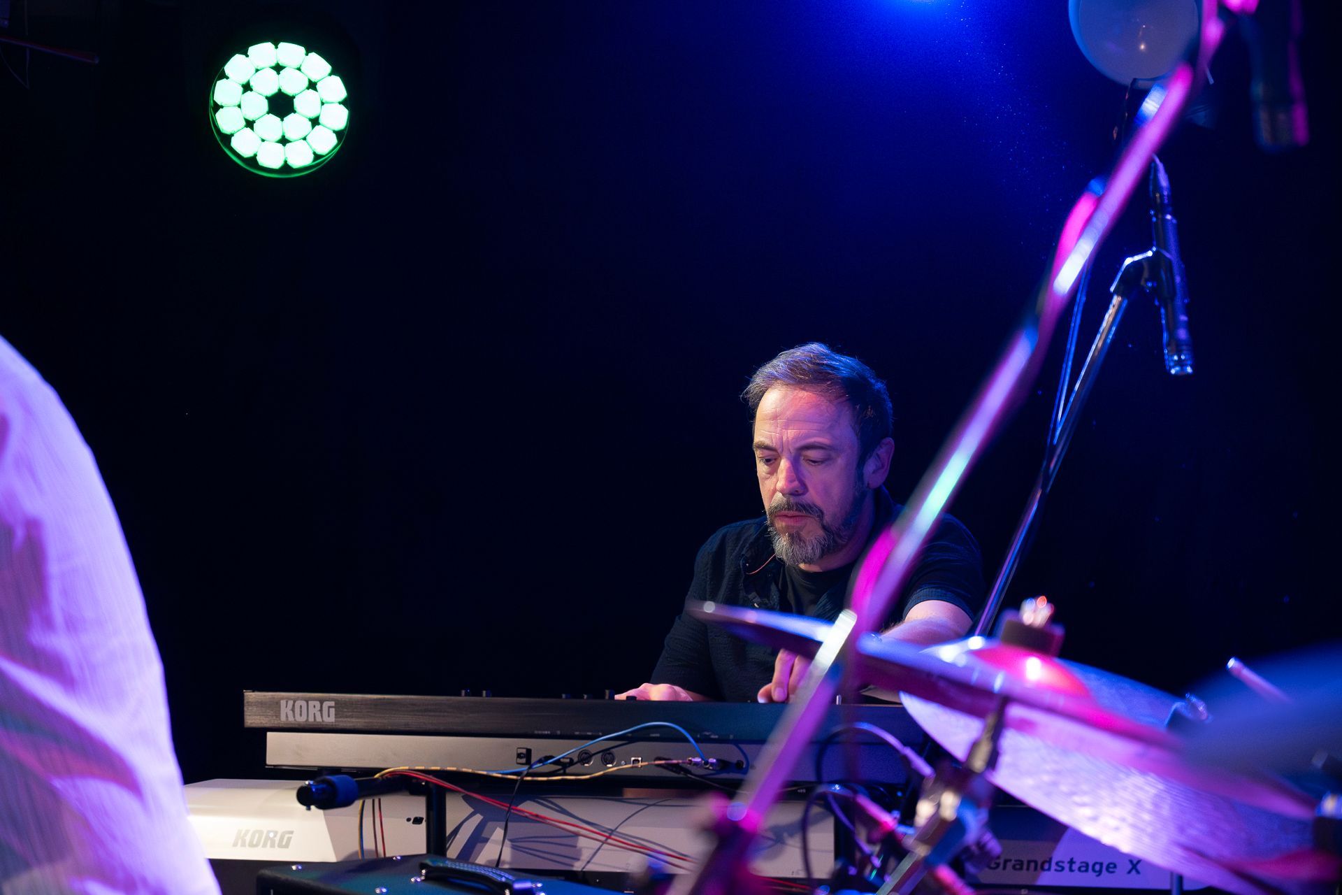 Keyboarder spielt auf der Bühne, schwarzes Hemd, dunkle Umgebung, Bühnenbeleuchtung, Instrumente.