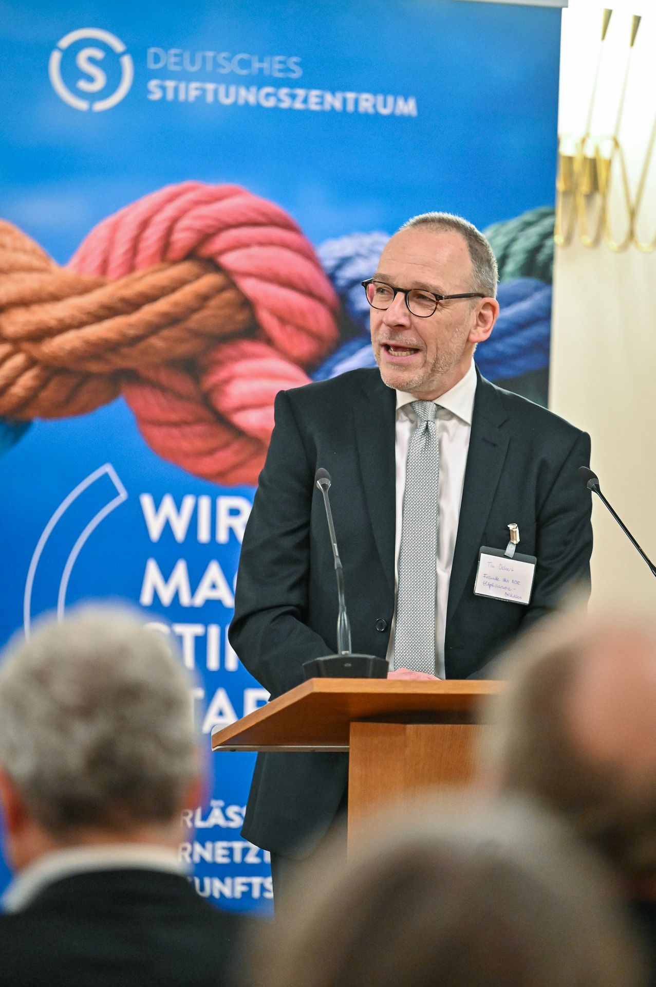 Man speaking at a podium with banner for Deutsches Stiftungszentrum.