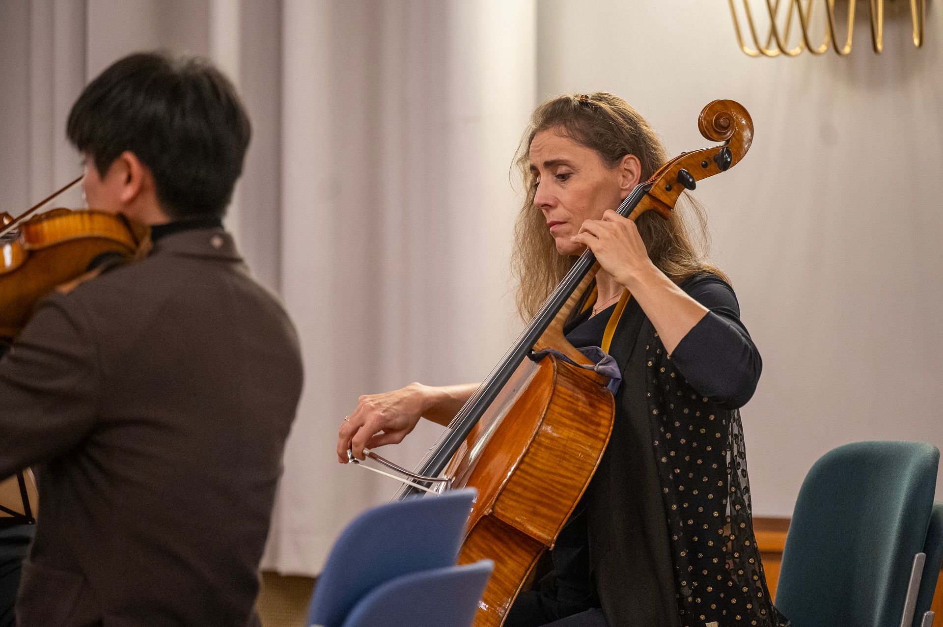 Ein Cellist spielt Cello. Ein Geiger ist teilweise zu sehen und spielt Geige. Innenaufnahme.