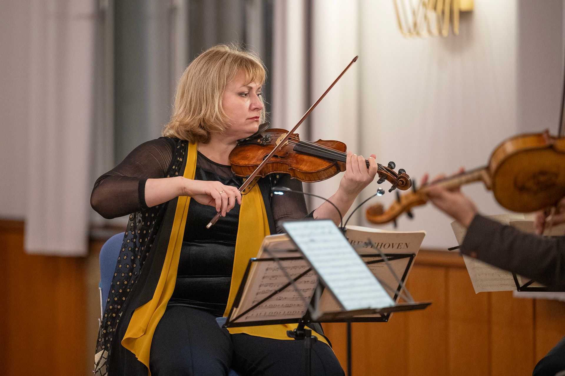 Frau, die in Schwarz und Gelb gekleidet Geige im Orchester spielt, mit Notenblättern.