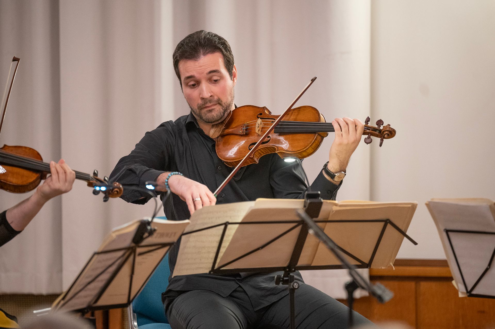 Ein Mann spielt konzentriert Geige und liest Noten in einem Konzertsaal.