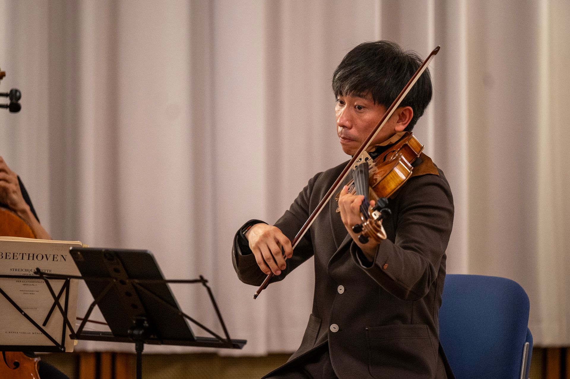 Ein Musiker spielt auf der Bühne Geige, hält dabei einen Bogen und betrachtet das Instrument.