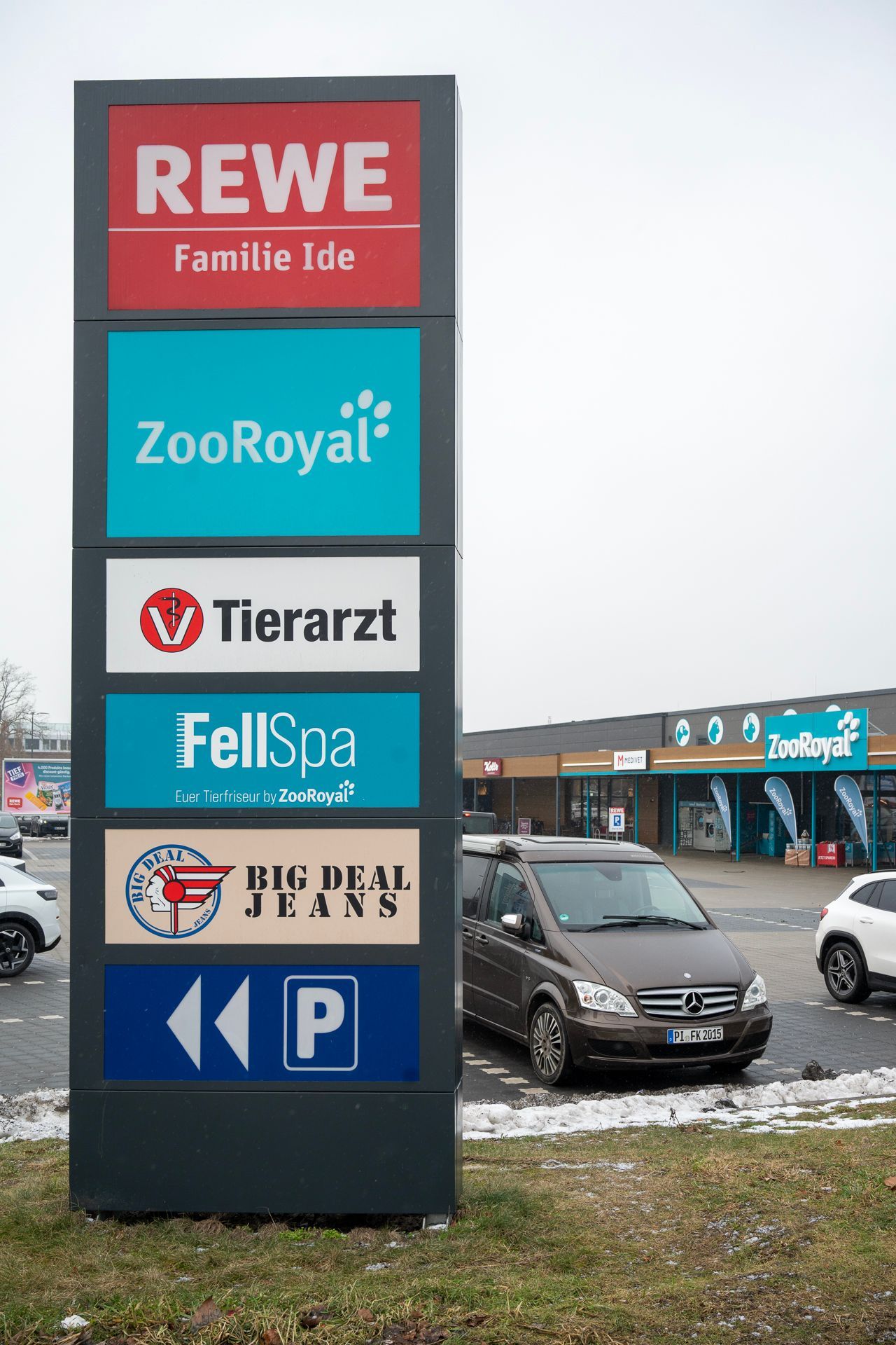 Wegweiser für den REWE-Markt mit verschiedenen Ladenlogos, darunter ZooRoyal, Tierarzt und Parkplatz.