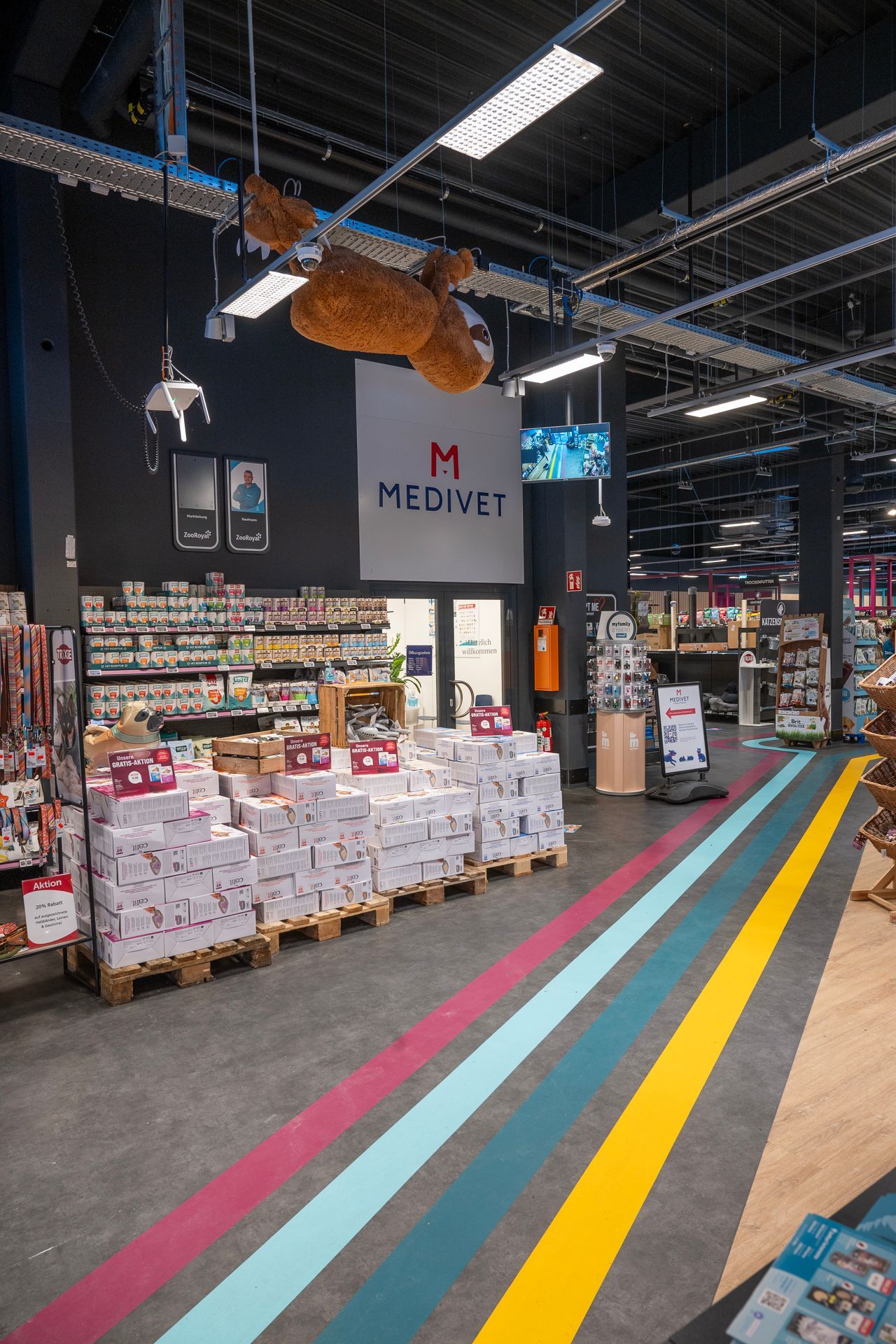 Innenansicht eines Ladens mit Warenauslagen, bunten Bodenstreifen und einem Schild mit der Aufschrift „MEDIVIT“.