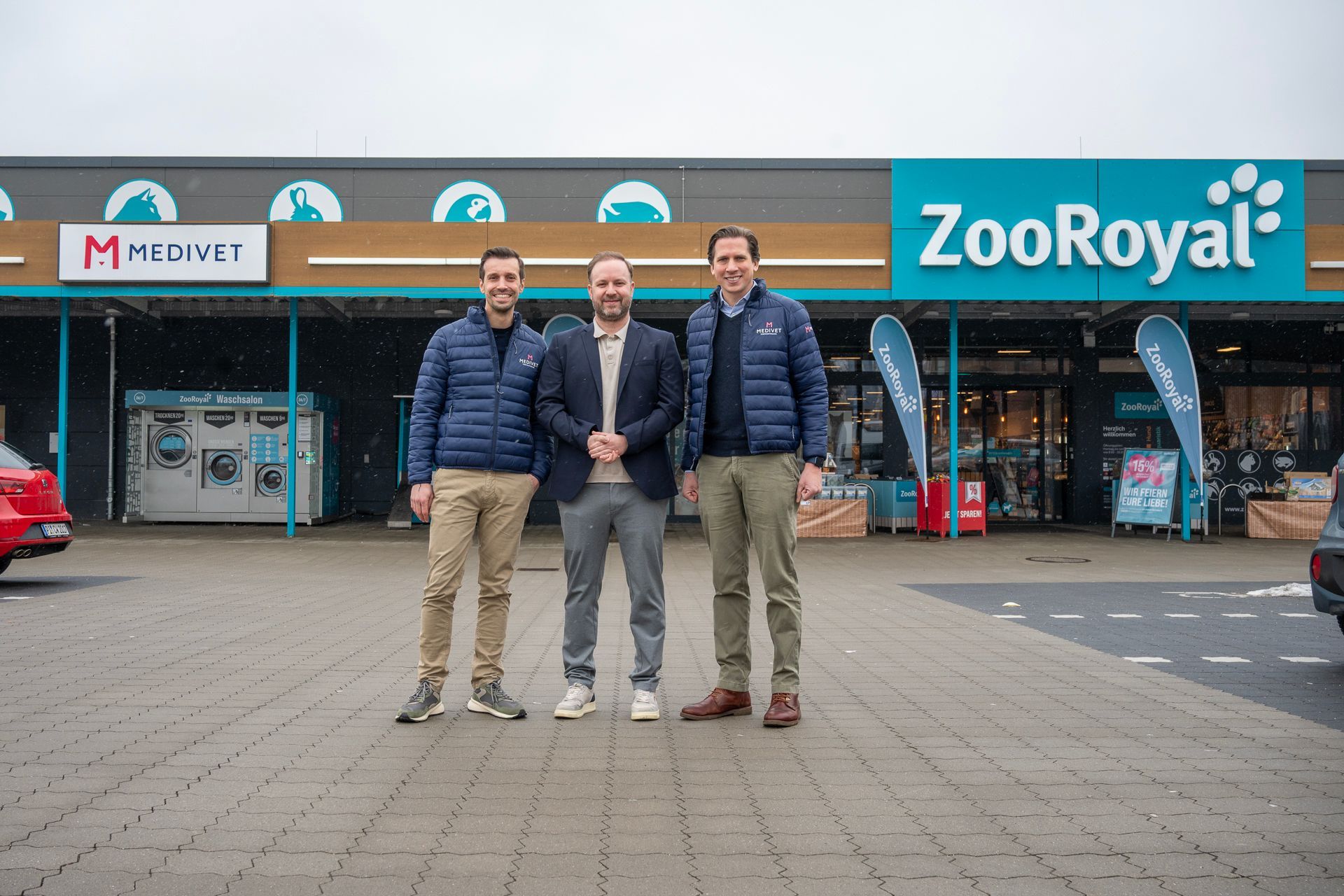 Drei Männer stehen vor einem Tiergeschäft; Schilder mit der Aufschrift „ZooRoyal“ und „MED VET“ sind gut zu sehen.